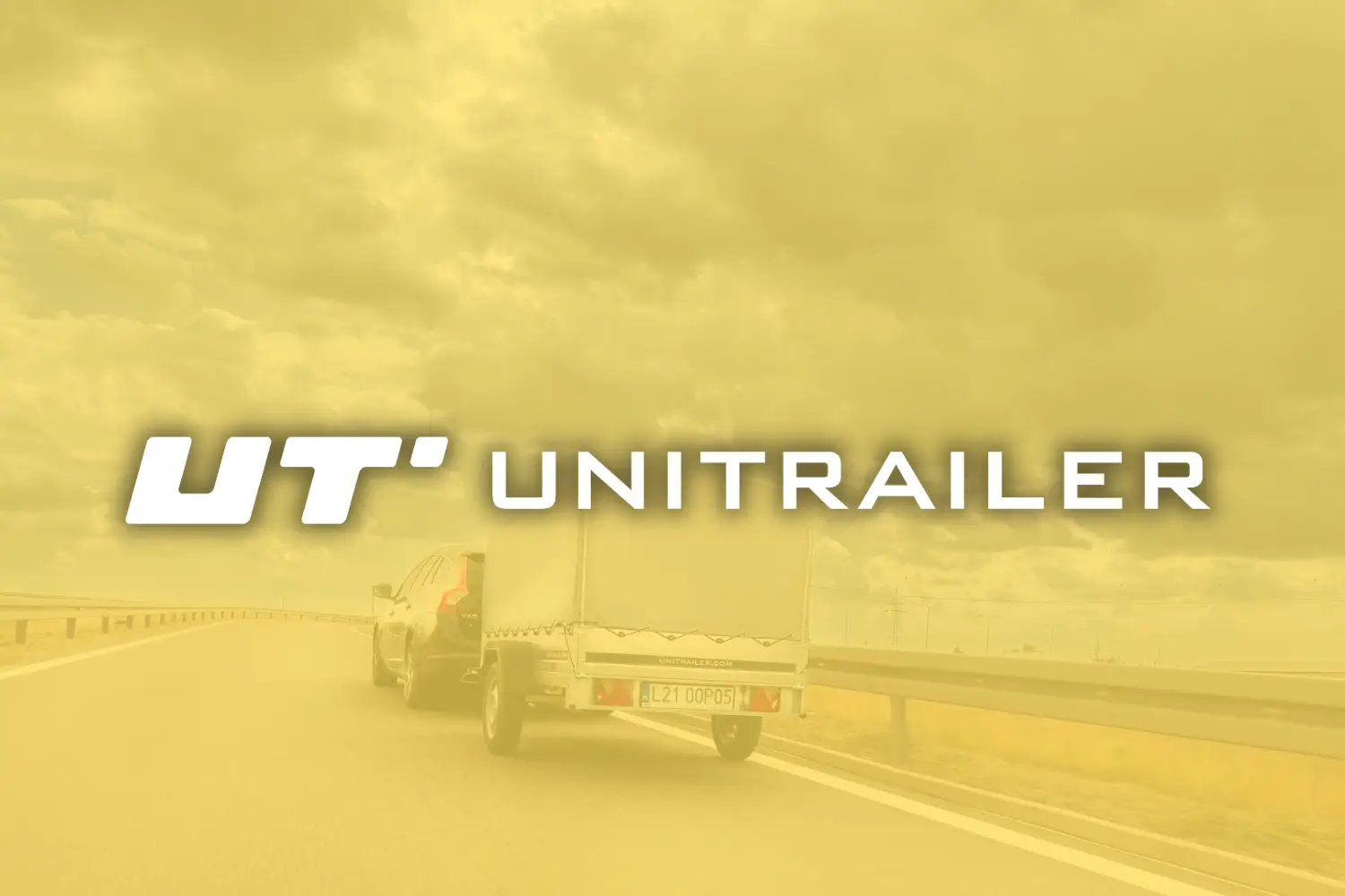 Visuel publicitaire ou vignette de présentation stylisée, entièrement recouverte d'un filtre transparent jaune ambré. Au centre de l'image, le logo de la marque « UT UNITRAILER » est écrit en lettres capitales blanches, épaisses et modernes, avec un léger effet d'ombre pour le détacher du fond. Derrière ce filtre jaune, on aperçoit un SUV sombre en train de rouler sur une autoroute à double voie, tractant une remorque routière équipée d'une bâche haute de couleur claire. Sur la ridelle arrière de la remorque, on peut lire l'immatriculation polonaise « L21 0OP05 » et l'adresse internet « UNITRAILER.COM ». La route est bordée d'une glissière de sécurité métallique et de champs à perte de vue sous un ciel lourd et nuageux.